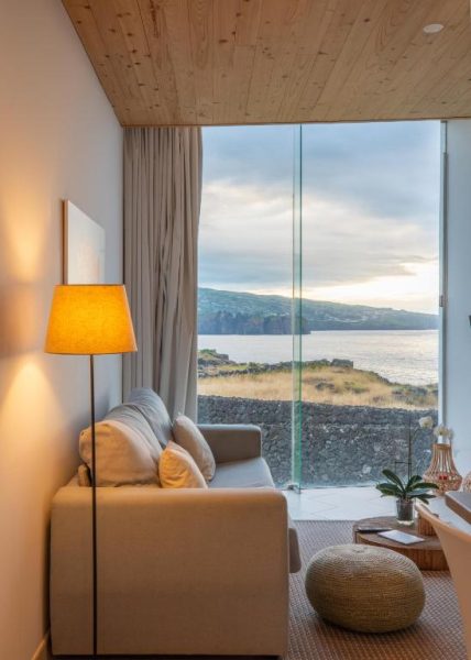 Salón con sofá y ventanal panorámico con vistas al mar y acantilados en Sao Vicente Lodge Atlantic Retreat