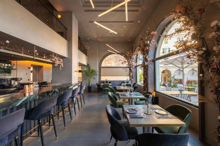 Restaurante y barra de bar con decoración floral y ventanales arqueados en el Arcadion Hotel
