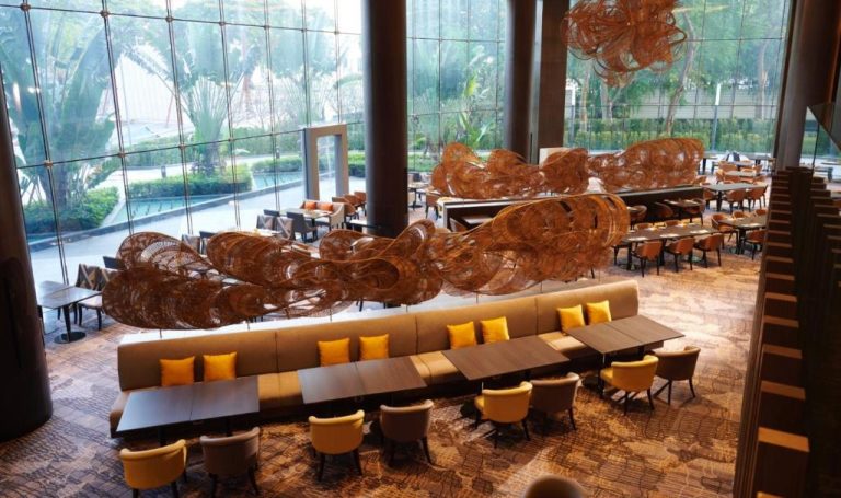 Restaurante del Chatrium Grand Bangkok con sofás, sillas amarillas y escultura decorativa de mimbre suspendida