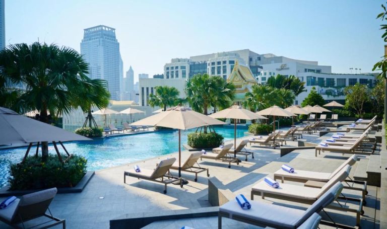 Piscina exterior con tumbonas y sombrillas del Chatrium Grand Bangkok con vistas al skyline de la ciudad