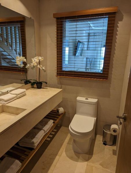 Baño de mármol con inodoro, lavabo y orquídeas blancas en Hacienda Samana Bay Hotel