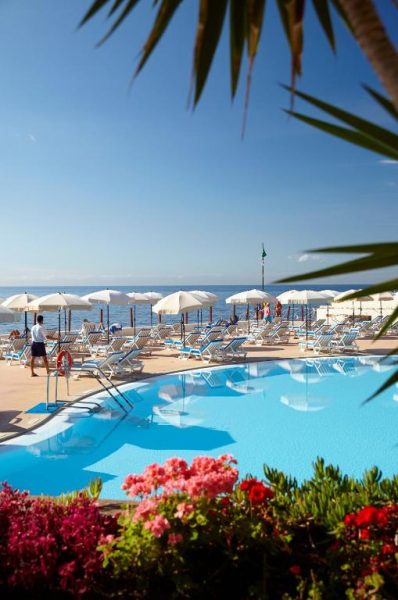 Piscina exterior con tumbonas y sombrillas frente al mar en The Cliff Bay PortoBay Madeira