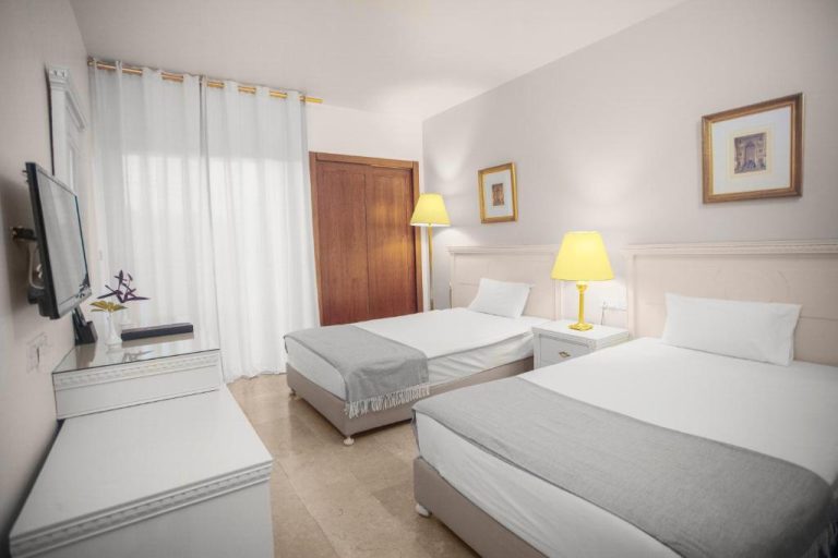 Habitación triple con dos camas individuales y decoración clásica en blanco del Grand Hotel Madaba