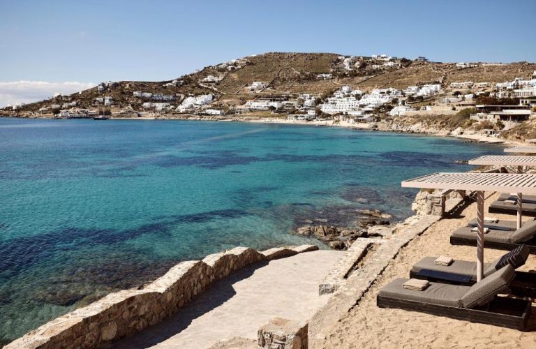 Playa cristalina con tumbonas y vistas al pueblo blanco desde Amazon Mykonos Resort and Spa