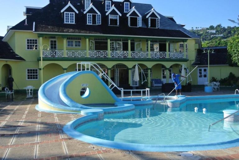 Piscina exterior con tobogán acuático y villa colonial amarilla en Deluxe SandCastles Condos Jamaica