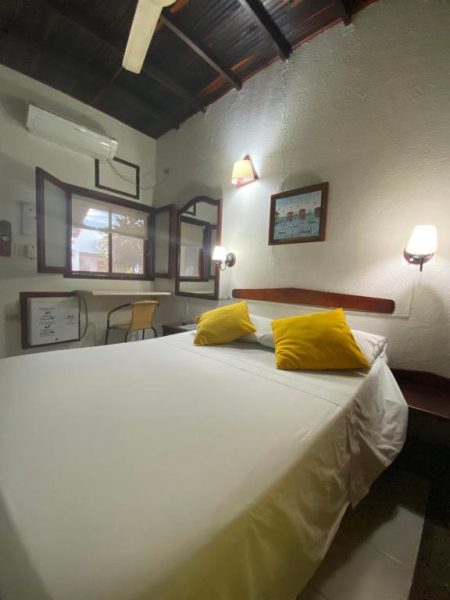Habitación doble con cama matrimonial y cojines amarillos en Hotel Nueva Granada