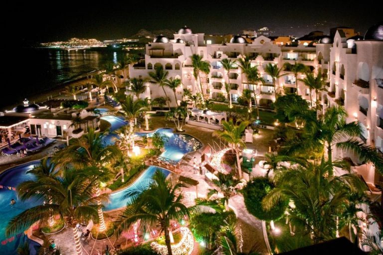 Vista nocturna de las piscinas y jardines tropicales del Pueblo Bonito Los Cabos Blanco Beach Resort con palmeras iluminadas