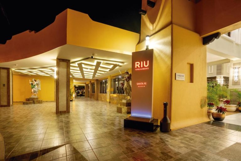 Entrada principal e iluminada del Hotel Riu Santa Fe All Inclusive con zona de check-in y esculturas decorativas