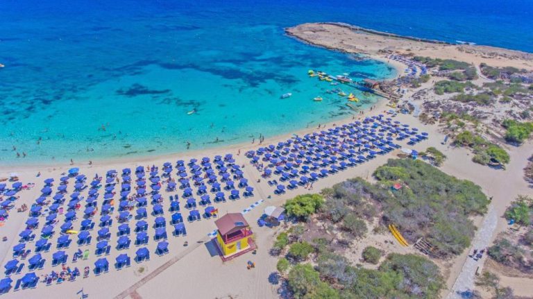 Vista aérea de la playa con sombrillas azules y aguas cristalinas del Tsokkos Paradise Holiday Village en Chipre