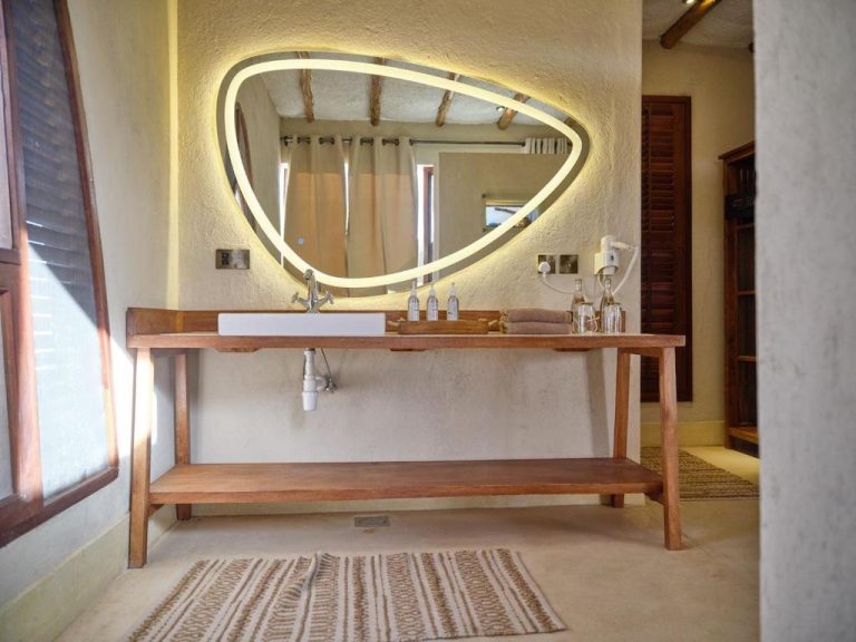 Baño de diseño con lavabo sobre mueble de madera y espejo LED triangular en Surana Buffalo Springs