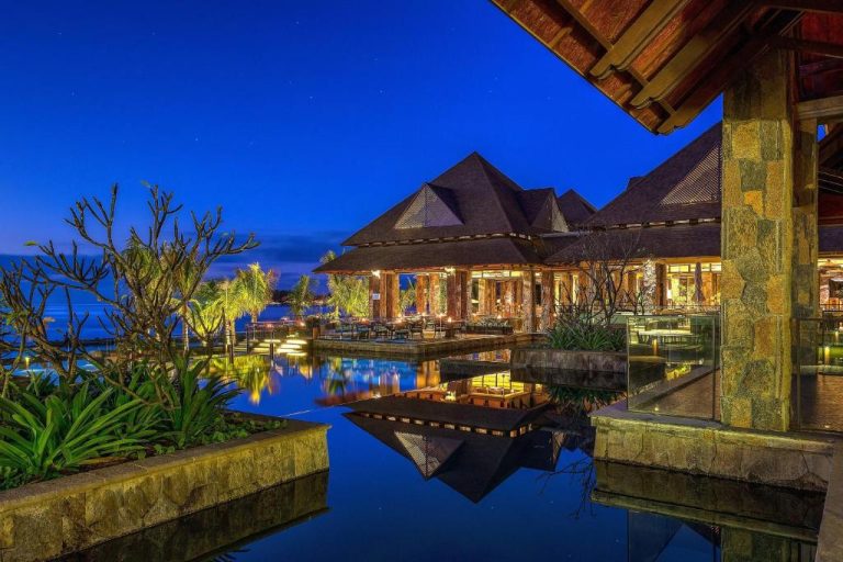 Restaurante sobre piscina reflejante iluminado de noche en The Westin Turtle Bay Resort & Spa Mauritius