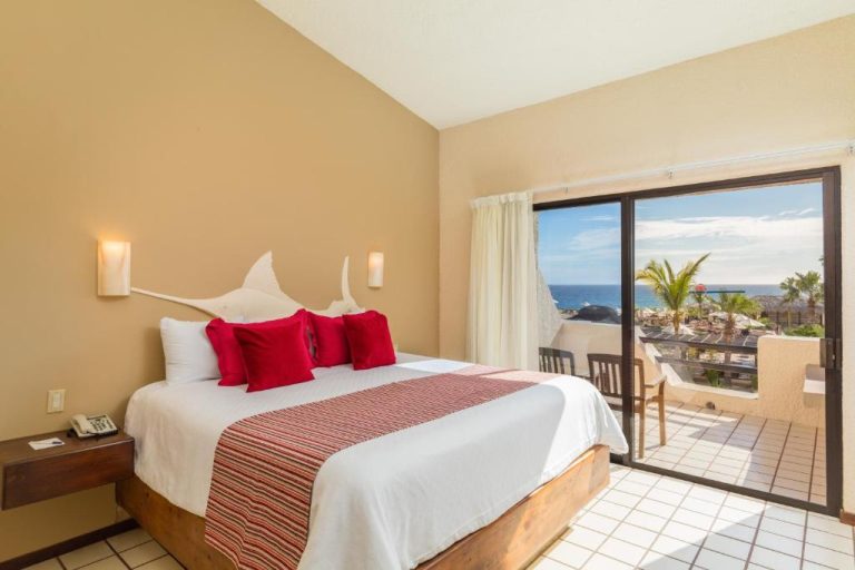 Habitación con cama king, almohadas rojas y balcón con vista al mar en Solmar Resort Los Cabos