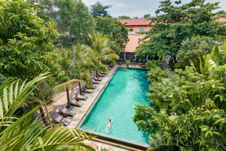 Piscina exterior rodeada de jardín tropical con tumbonas en Plantation Urban Resort & Spa