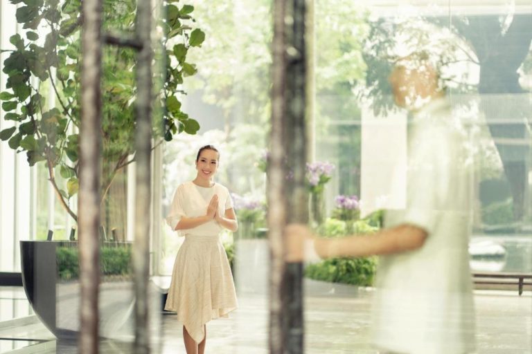 Recepcionista en el lobby del Four Seasons Hotel Bangkok dando la bienvenida con gesto tradicional tailandés