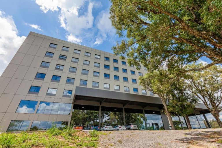 Fachada exterior moderna del Tri Hotel Antônio Prado con estacionamiento y árboles alrededor