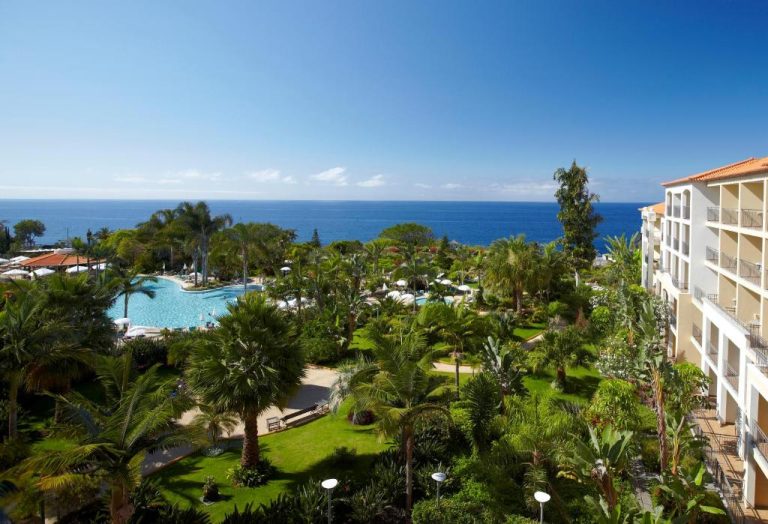 Piscina exterior rodeada de jardines tropicales con vistas al mar en el Hotel Porto Mare PortoBay