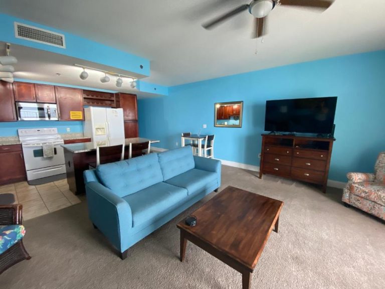 Sala de estar con sofá azul y cocina integrada en el apartamento Laketown Wharf Panama City Beach