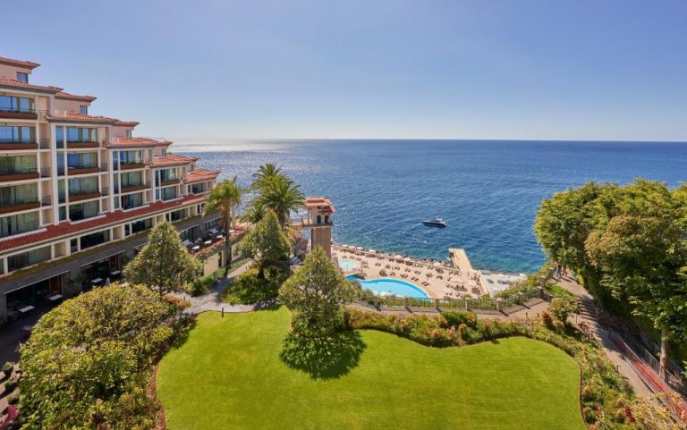 Vista aérea de la piscina exterior y jardines del hotel The Cliff Bay PortoBay con vistas al océano Atlántico