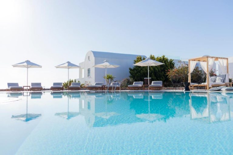 Piscina exterior con tumbonas y sombrillas blancas del Astro Palace Hotel & Suites en Santorini