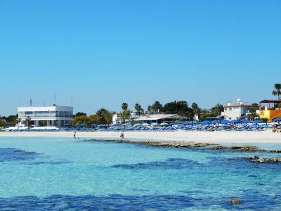 Playa de aguas cristalinas turquesas frente al Tsokkos Paradise Holiday Village con tumbonas y sombrillas azules