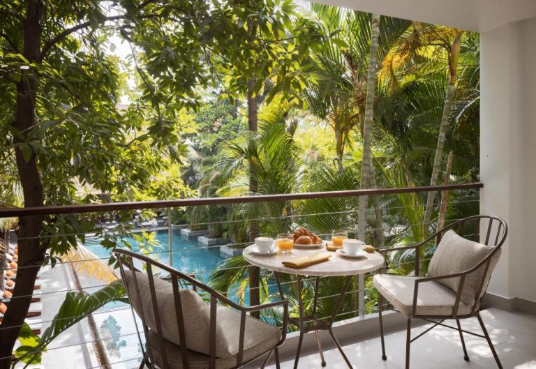 Balcón privado con desayuno y vistas a la piscina rodeada de jardín tropical en Plantation Urban Resort & Spa