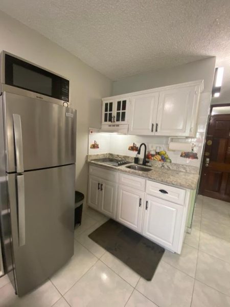 Cocina equipada con nevera de acero, fregadero y armarios blancos en Ocho Rios Vacation Resort
