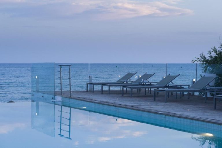 Piscina infinita con tumbonas y vistas al mar al atardecer en The Sindbad Hotel