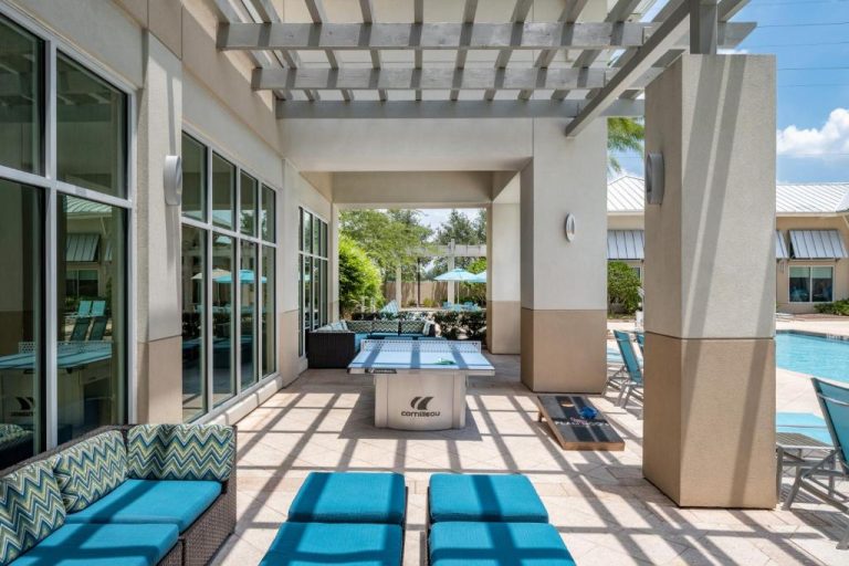 Terraza cubierta con ping pong y tumbonas azules junto a la piscina del SpringHill Suites Flamingo Crossings Orlando