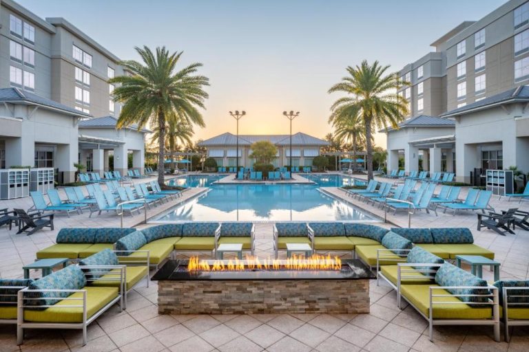 Piscina exterior con tumbonas azules y zona de fogón del SpringHill Suites Orlando Flamingo Crossings al atardecer