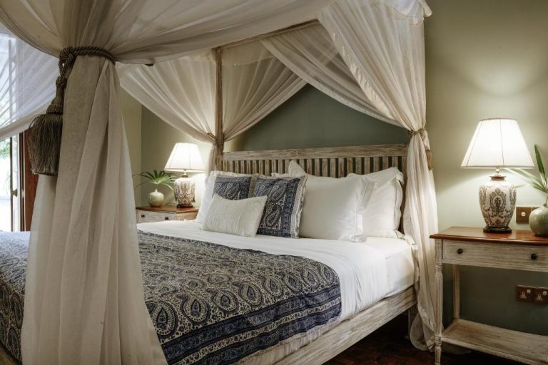 Habitación con cama de dosel de madera y cortinas blancas en el Maniumpathy Hotel