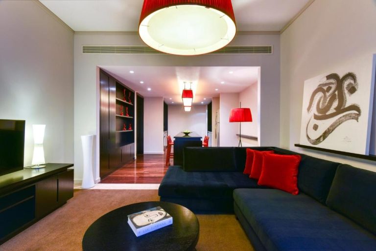 Lujoso salón de suite en W Doha con sofá azul, cojines rojos y comedor al fondo