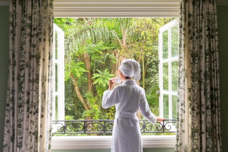 Mujer en bata blanca disfrutando de la vista al jardín tropical desde su habitación en Palácio Tangará