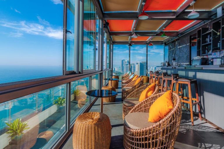 Terraza bar panorámica con sillas de mimbre y vistas al mar y ciudad en Le Sands Oceanfront Danang Hotel