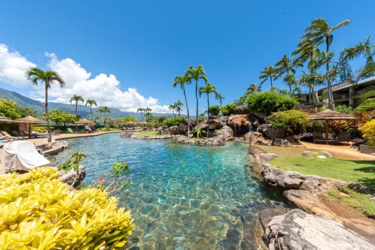 Piscina laguna natural con rocas y cascada del Hanalei Bay Resort rodeada de palmeras en Kauai
