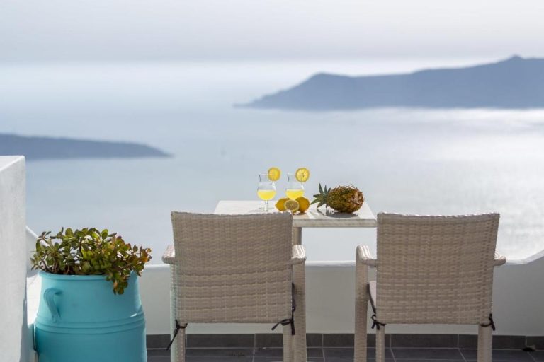 Terraza con mesa y sillas de ratán en Remvi Suites con vistas panorámicas al mar Egeo en Santorini