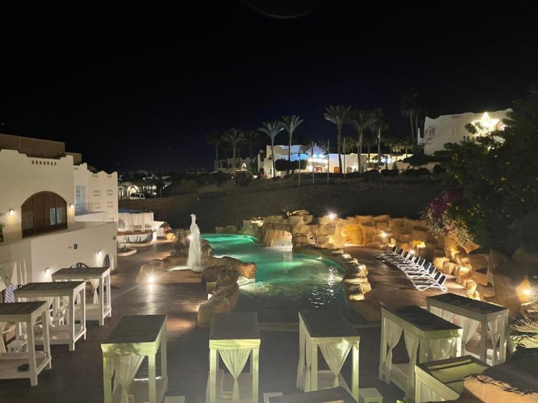 Piscina con fuente y rocas iluminada de noche en Elisir SPA & Hotel en Sheikh coast