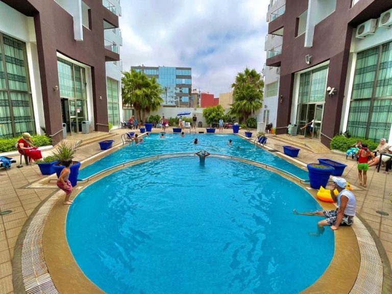 Piscina exterior con forma ovalada y tumbonas del Appart Hôtel Founty Beach rodeada de edificios