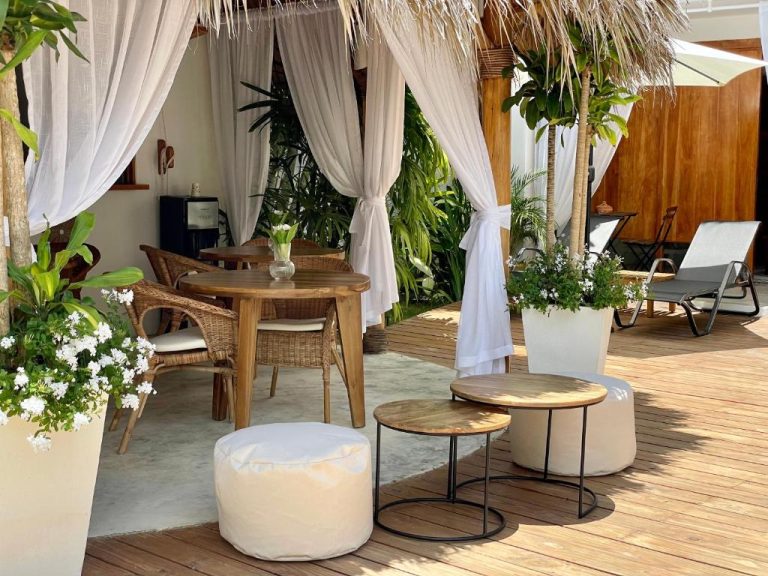 Terraza con cabana tropical y mobiliario de ratán en Leeloo Boutique Hotel, rodeada de plantas y flores blancas