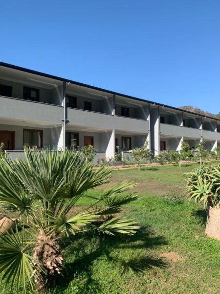 Fachada exterior y jardín con palmeras del Hotel Doga Ciftlik Konaklama bajo cielo azul