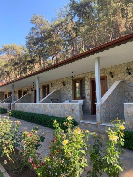 Fachada de piedra con jardín de rosas y terraza cubierta del hotel Doga Ciftlik Konaklama entre pinos