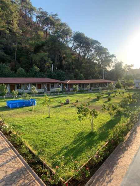 Jardín verde con piscina desmontable y bungalows rodeados de montaña en Doga Ciftlik Konaklama