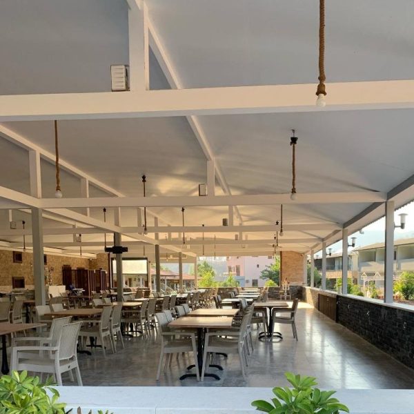 Terraza cubierta del restaurante Doga Ciftlik Konaklama con mesas y sillas blancas y techo estructural