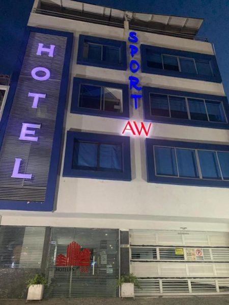 Fachada exterior iluminada del AW Hotel Sport con letreros de neón azul y rojo en la noche
