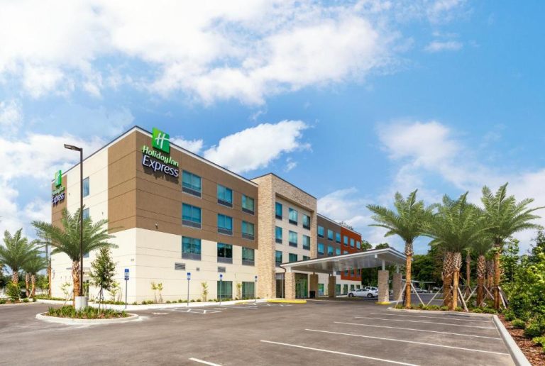 Fachada exterior del Holiday Inn Express Starke con aparcamiento y palmeras en un día soleado