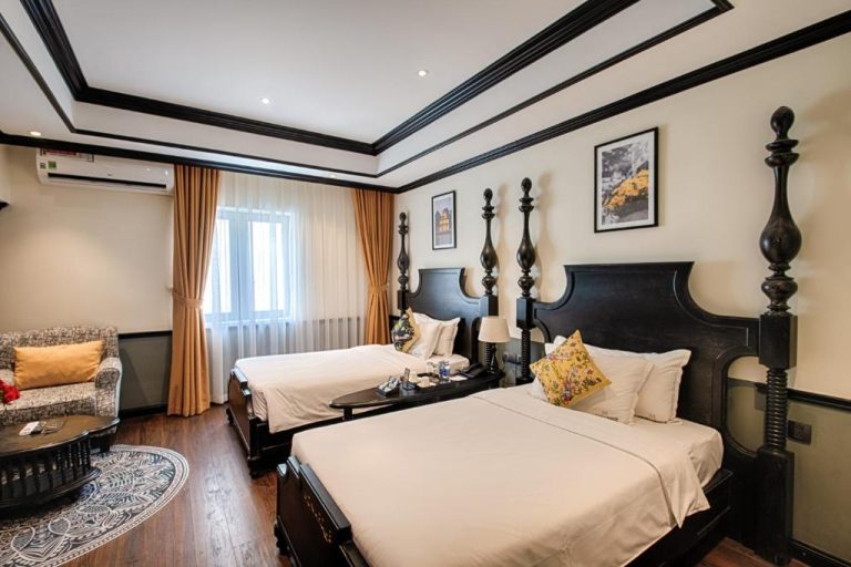 Habitación doble con camas de madera oscura estilo colonial en Monarque Hotel Danang, Vietnam