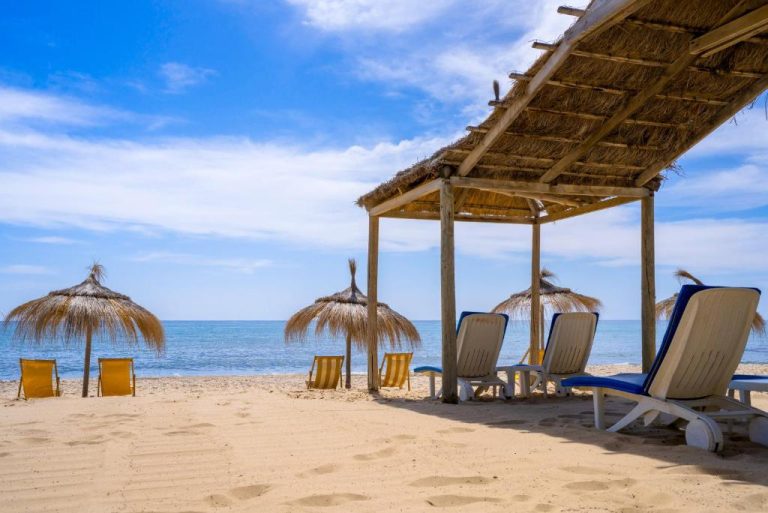 Playa privada con hamacas, sombrillas de paja y pérgola del Hotel Bel Azur Thalasso & Bungalows