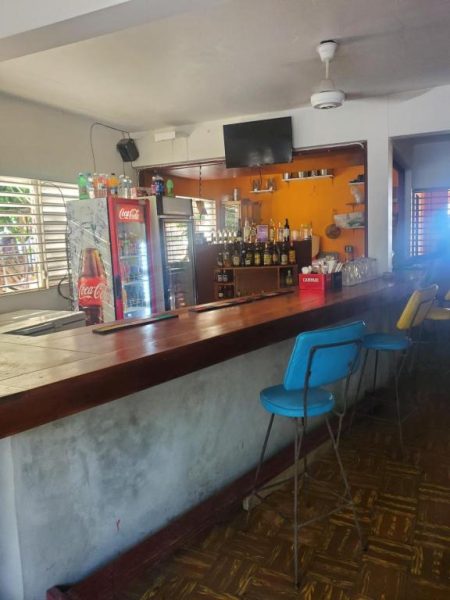 Bar con barra de madera, nevera Coca-Cola y estantes con botellas en Evelin's On The Beach