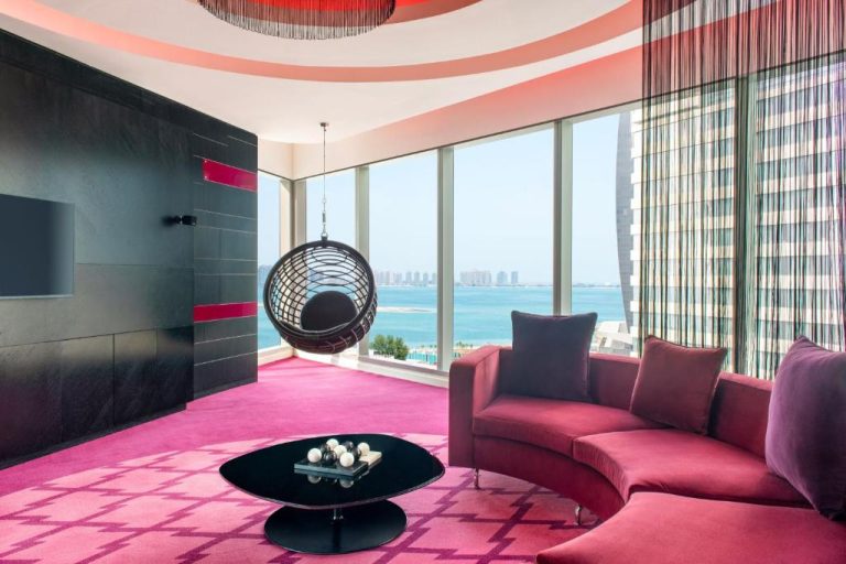 Suite de lujo con sofá curvo fucsia y silla colgante con vistas al mar en el W Doha