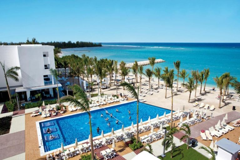 Piscina exterior con tumbonas y playa de aguas turquesas del Riu Palace Jamaica Adults Only All Inclusive