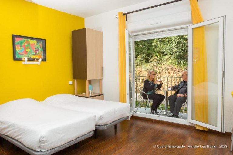 Habitación doble con pared amarilla y balcón con vistas al jardín en Appart'Hotel Castel Emeraude